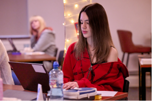A schoolgirl in a bright red hoodie works on a laptop in the classroom, focused on her screen