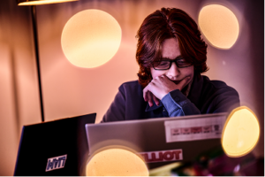 A schoolboy works on a laptop, his hand over his mouth as he concentrates deeply