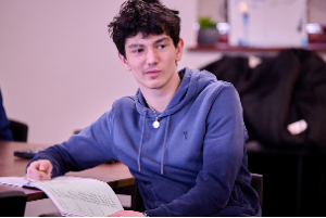 A schoolboy writes in his exercise book while looking up towards the whiteboard